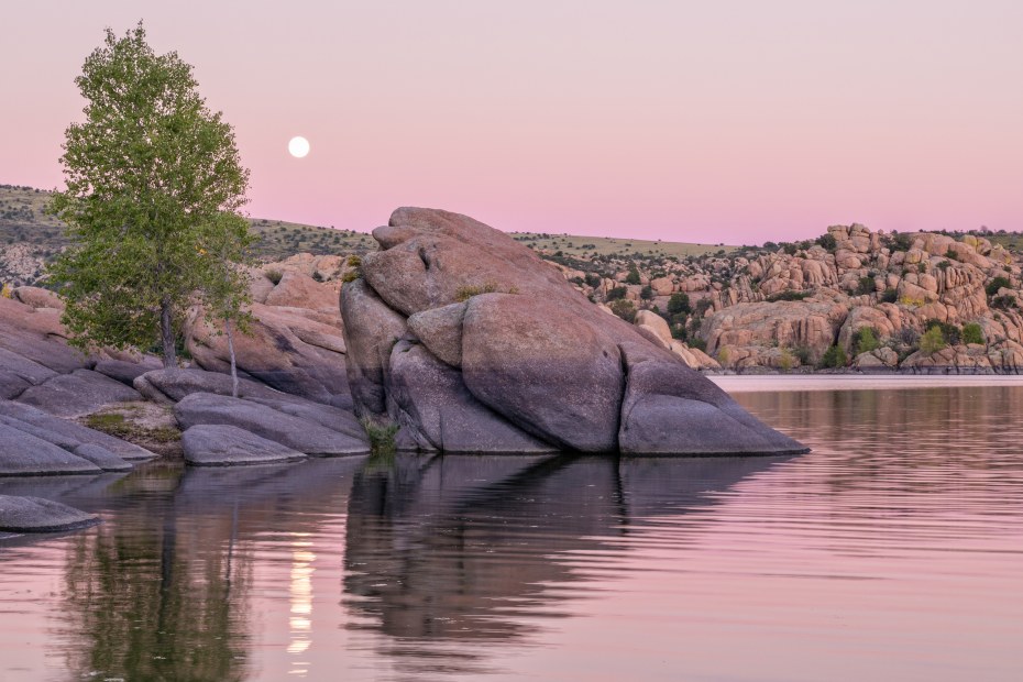 The moon rises over a pink sky relfected in Watson Lake near Prescott, Arizona.