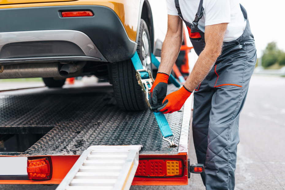 A tow truck driver secures an SUV to the back of a flatbed tow truck.