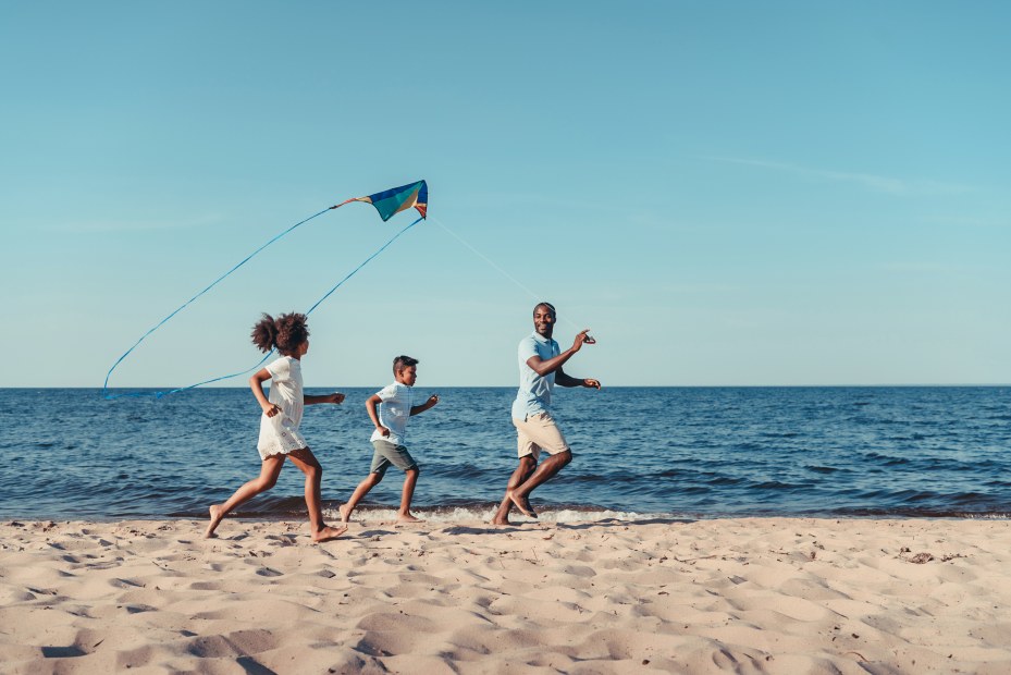 A family run down a beach together to get a kite to fly.