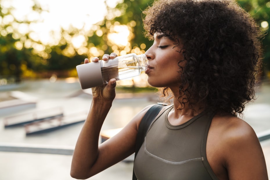 A woman drinks out of a glass water bottle on a hot day.