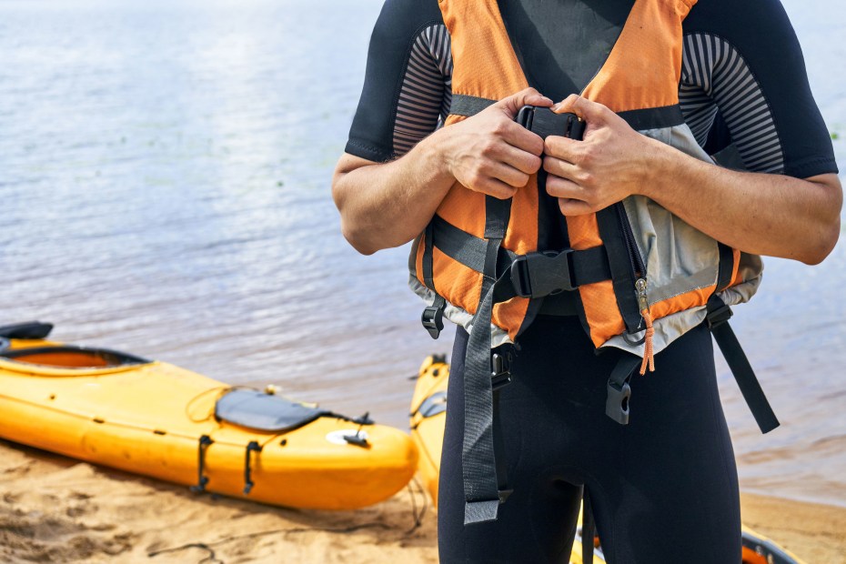 A person puts on their life jacket before getting into a canoe.