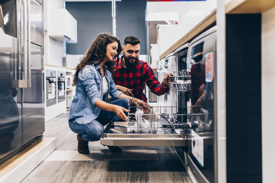A couple look inside a dishwasher at an appliance showroom.