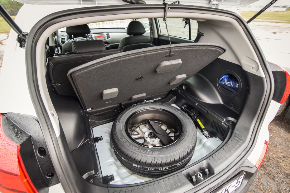 A spare tire in a storage compartment under an SUV trunk.