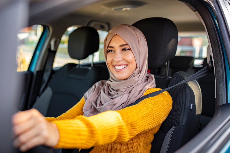 A woman smiles with both hands on the steering wheel.