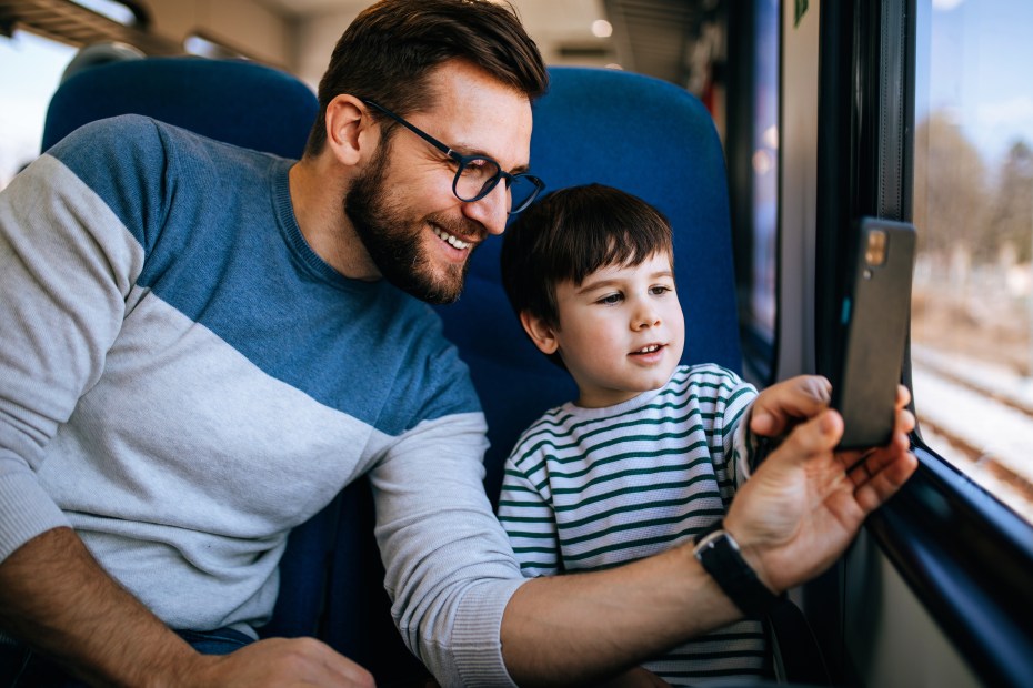 A father and his son look out a train window together.