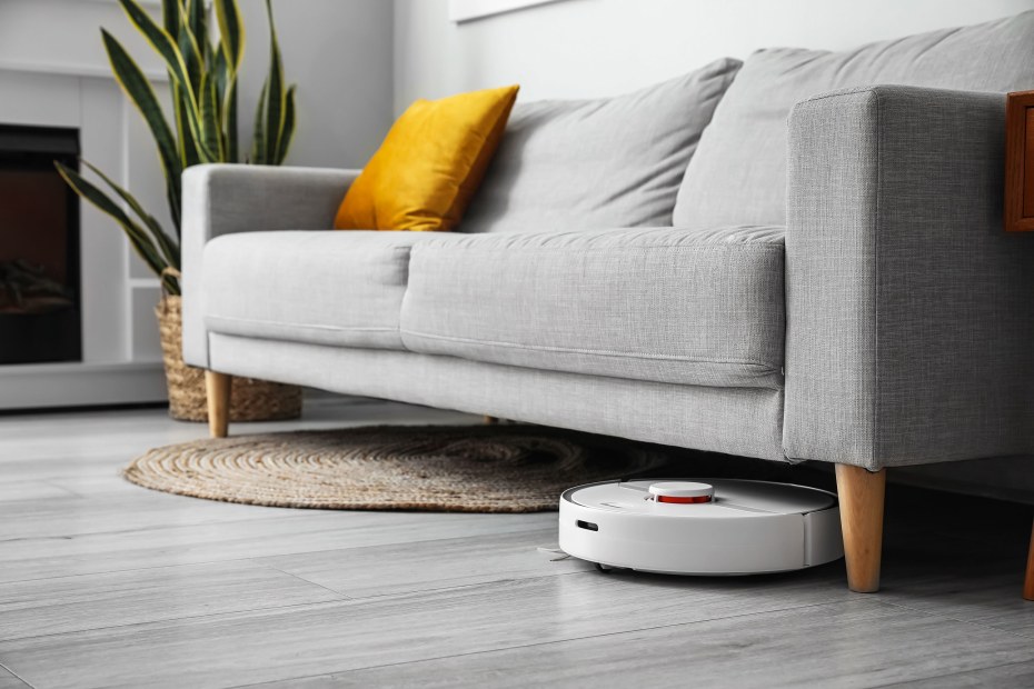 A smart robot vacuum cleans under a gray sofa.