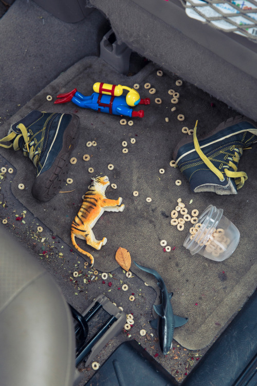 Kid's toys and cereal spilled on the floor of the back seat of a car.