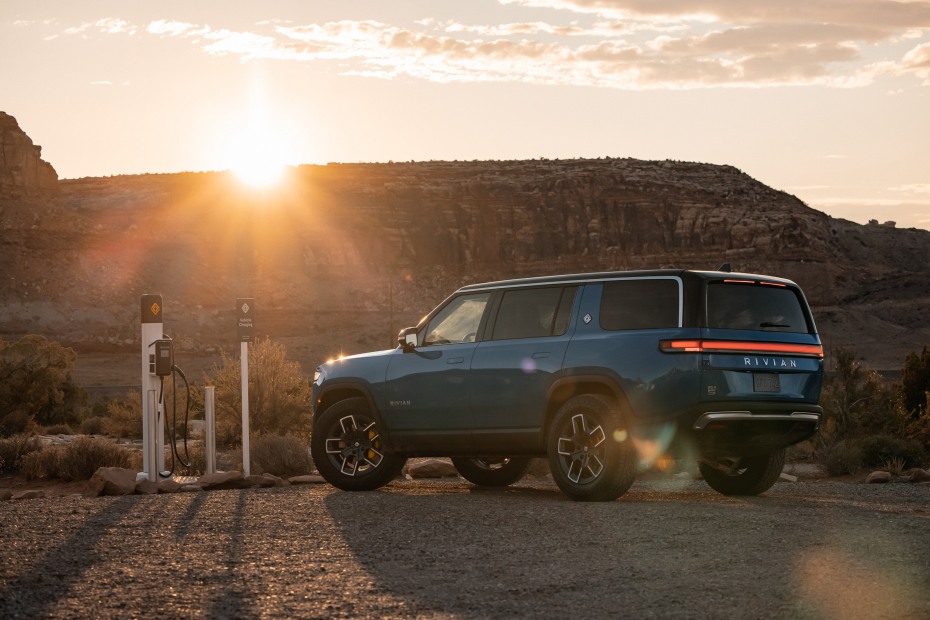 A Rivian R1S parked at a remote charging station near off-road trails.