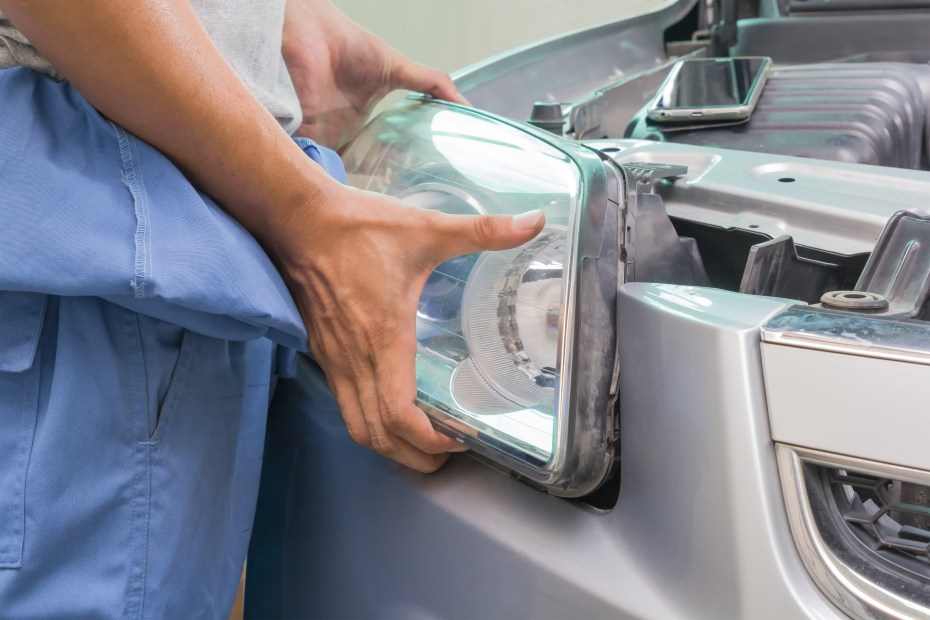 A mechanic replaces a headlight on a sedan.