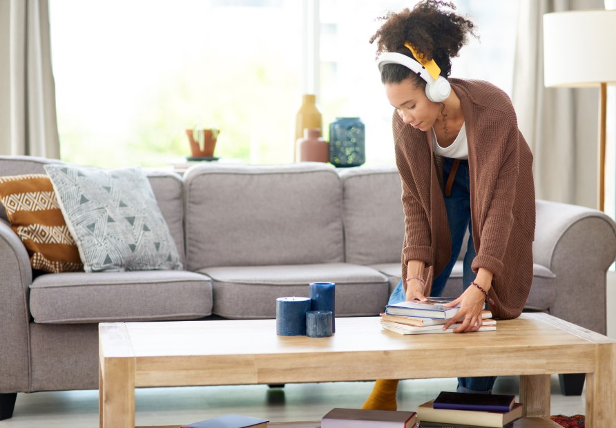 A woman cleans up clutter on the coffee table before guests arrive.