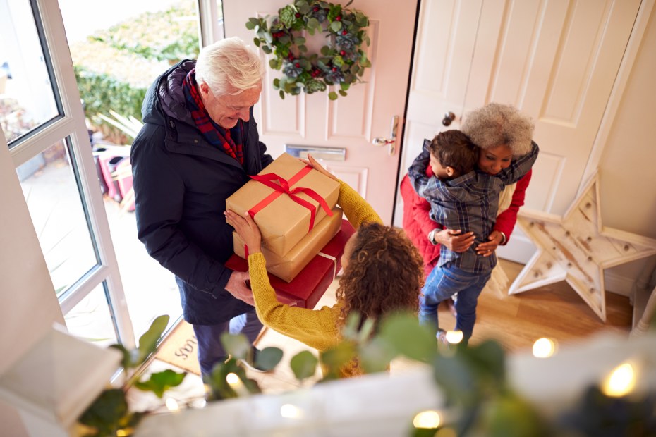 Two young grandkids greet their grandparents at the door with hugs.