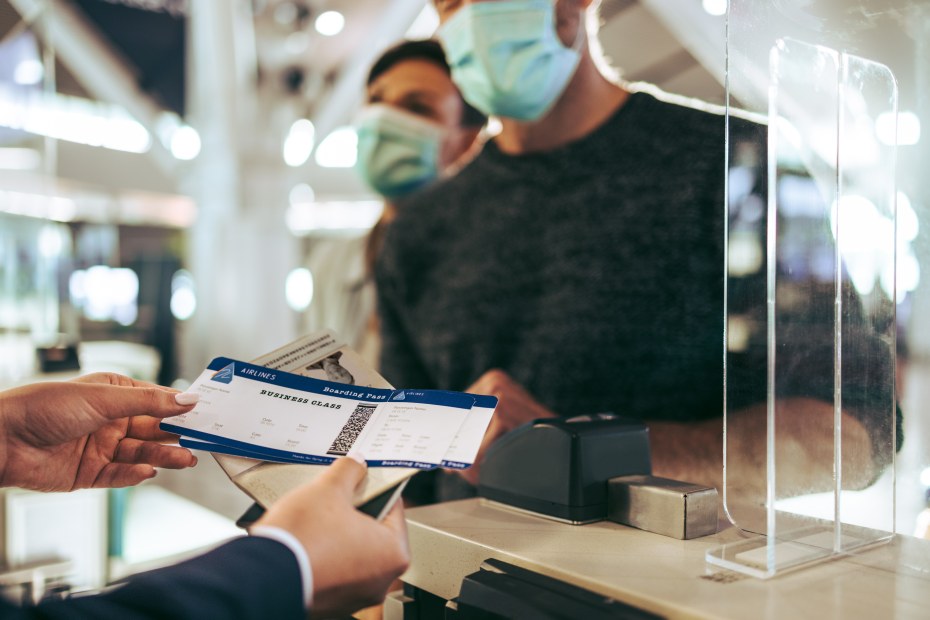 Two travelers pick up their boarding passes from the airport check-in counter.