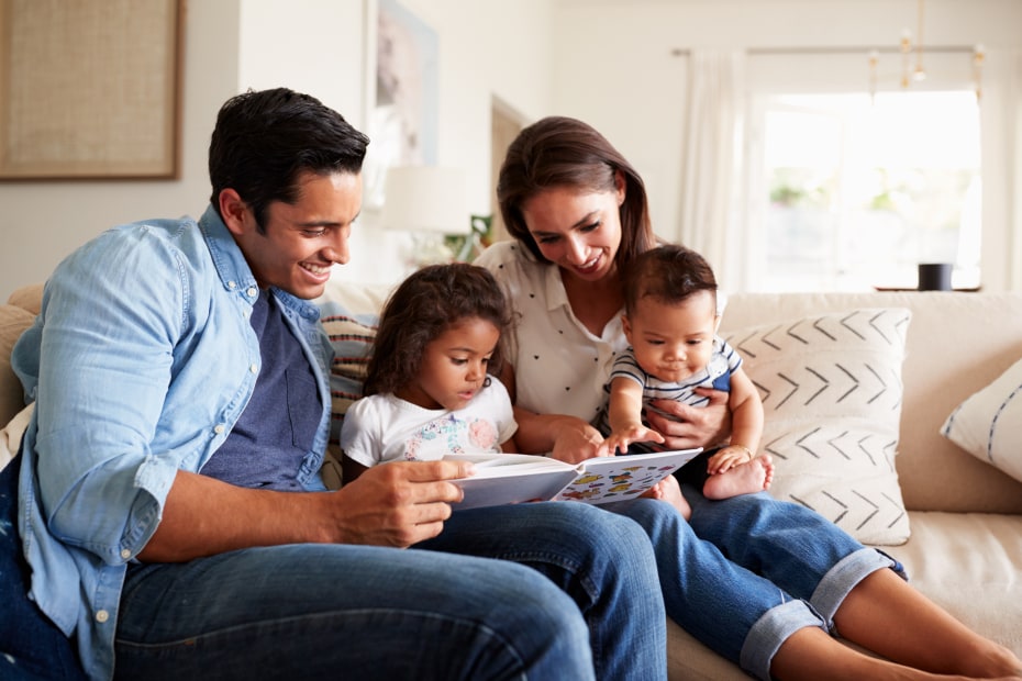 A family reads a picture book together on the couch.