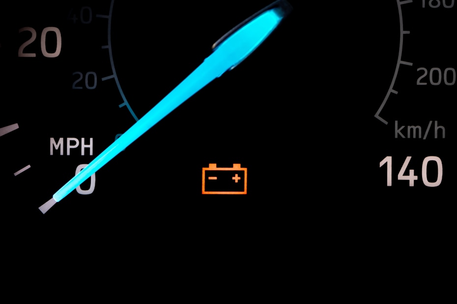 A battery warning light lit up on a close-up of a speedometer.