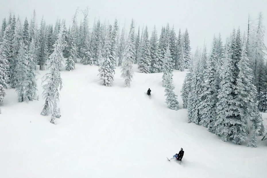 Two people ride snowmobiles during snowfall in Carbon County, Wyoming.