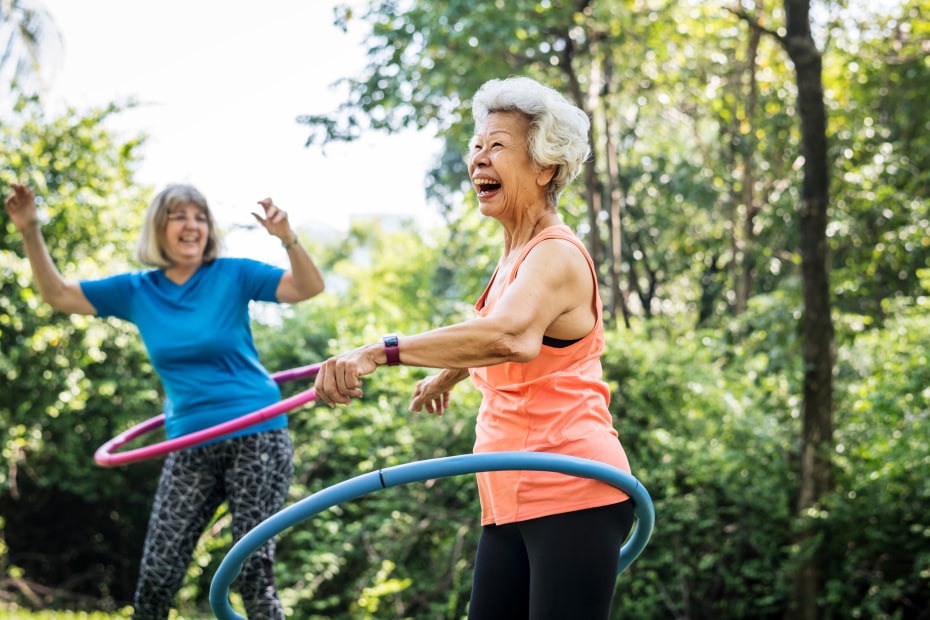 Two senior women hula hoop outside.