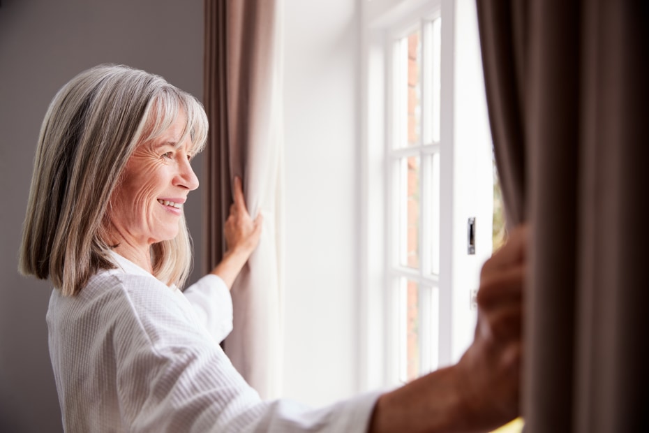 A woman looks out the open window in her home.