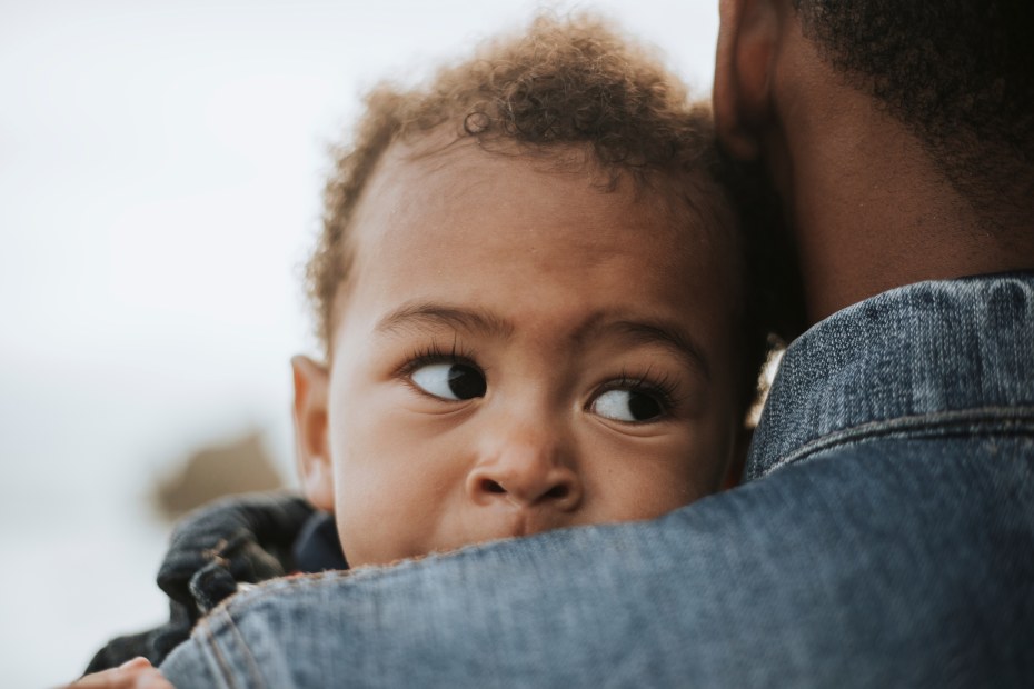 A baby looks over their parent's shoulder.