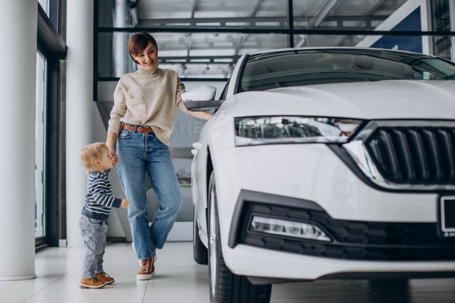 A mom and her son look at a white car in a car dealership showroom.