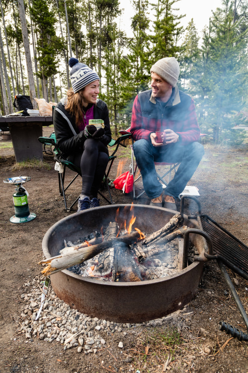 A couple sit around a campfire in a fire ring at Madison Campground, Yellowstone National Park.