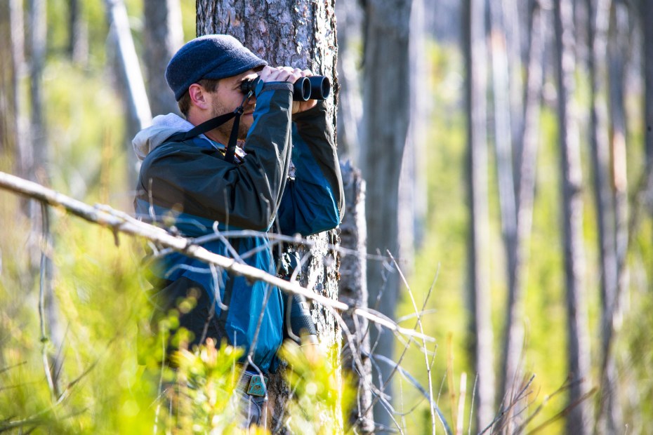A man looks through his binoculars at birds in Glacier National Park near Fish Creek.