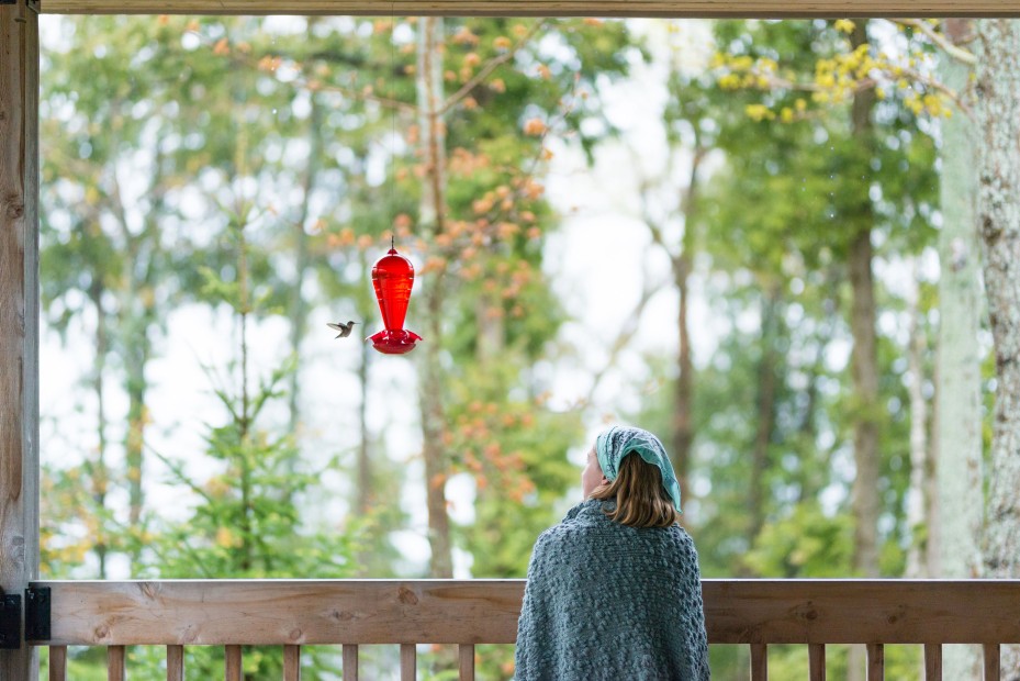 A girl watches a hummingbird fly to a feeder in her backyard.