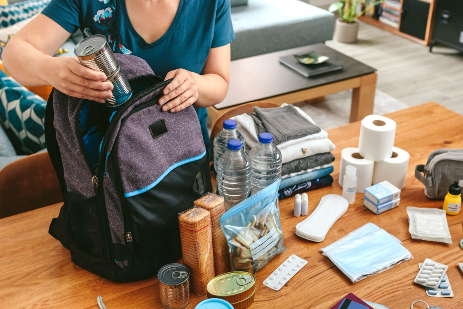 A woman packs an emergency kit backpack at her dining room table.