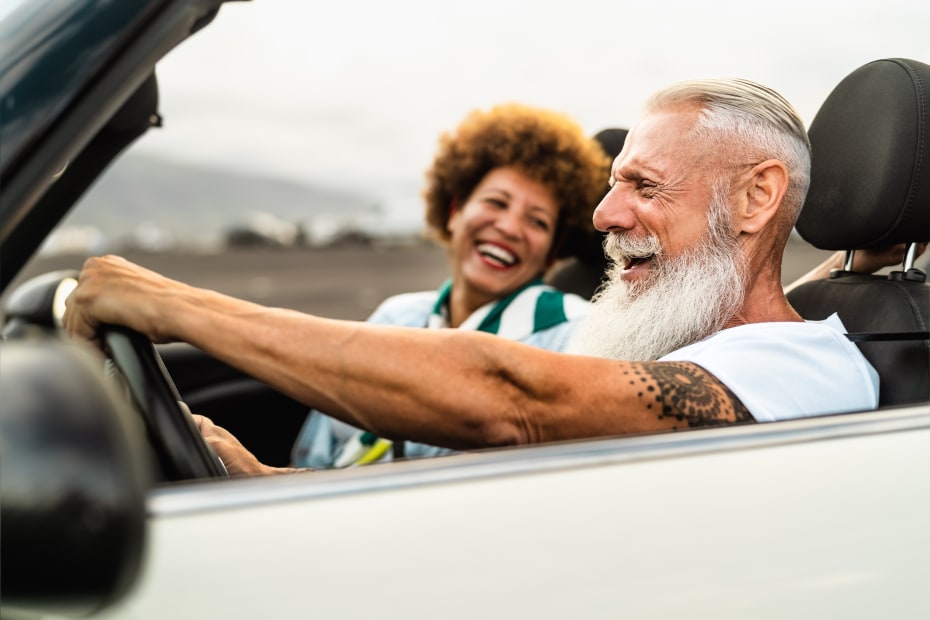A happy older couple smiles while riding in their white convertible.