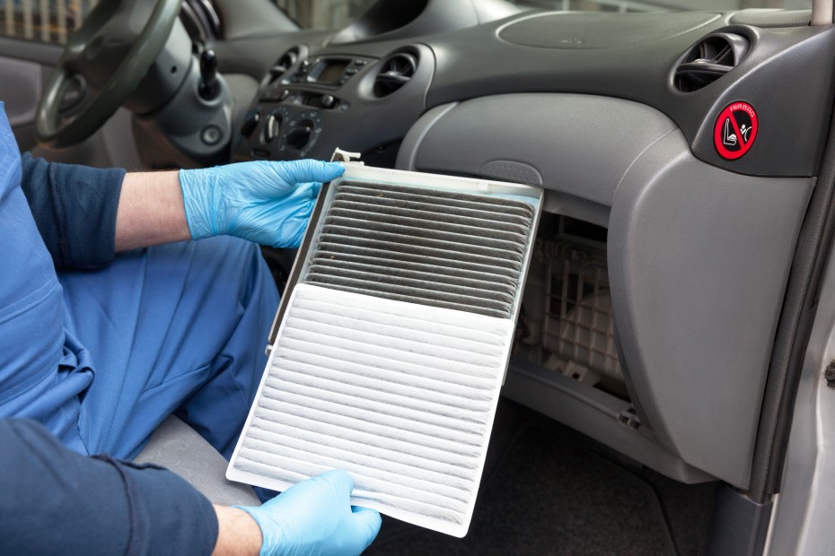 A mechanic changes the cabin air filter inside the glove box of a sedan.