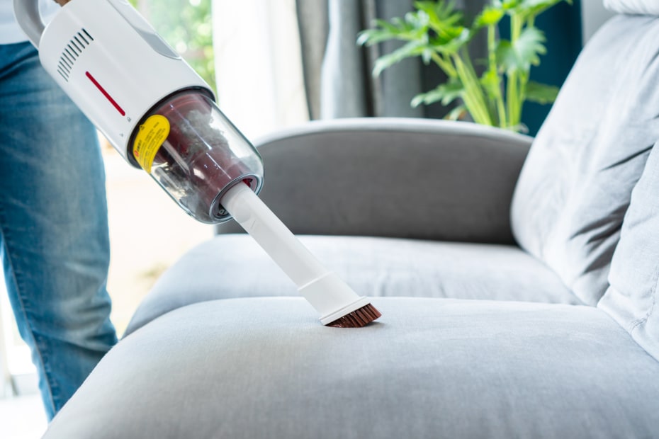 man uses a handheld vacuum to clean a couch cushion.
