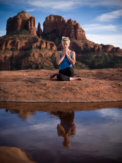 A woman meditates in front of Cathedral Rock and a reflecting pool in Sedona, Arizona.