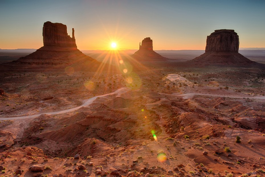 The sun rises between rock formations in Sunrise in Monument Valley, Utah.
