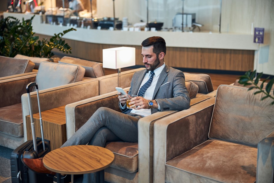 A man sits in an armchair with a cocktail inside an airport lounge.