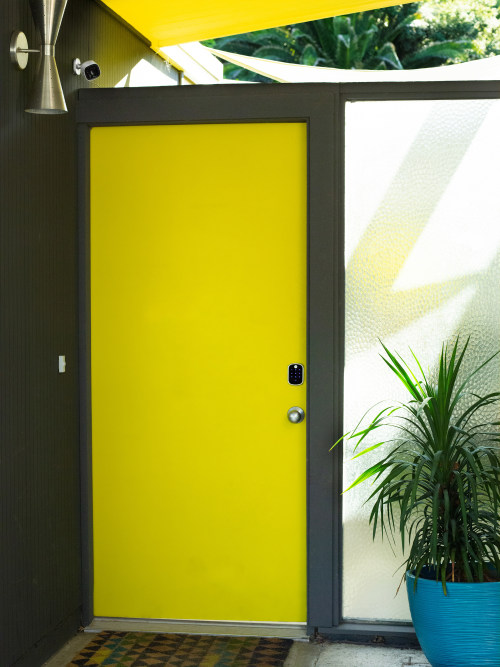 An outdoor security camera overlooks a porch and a smart lock on a yellow front door of a midcentury modern home.