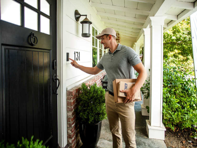 A delivery person rings a video doorbell before dropping off packages on the porch.