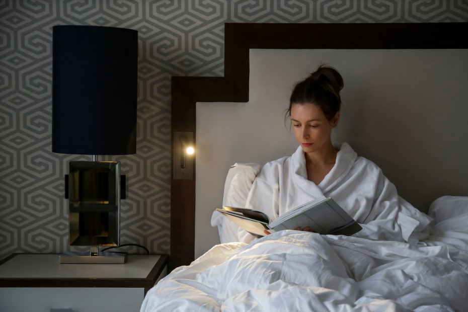 A woman reads her book in a hotel bed. 