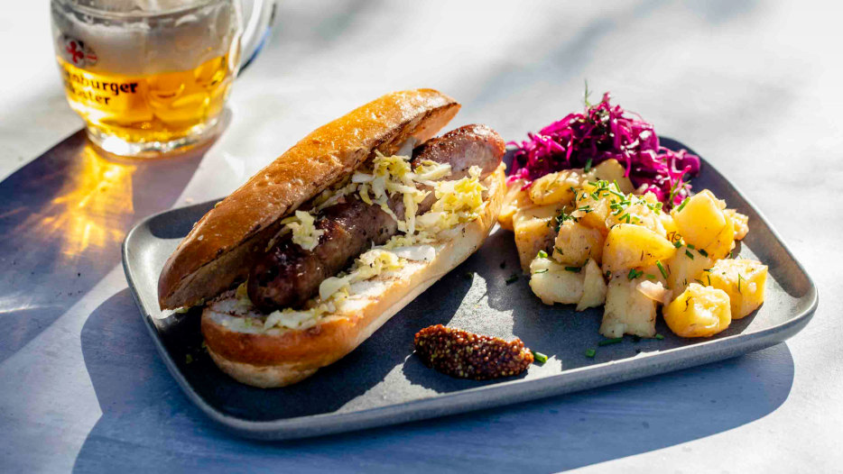 Bratwust with a side of warm potato salad, cabbage, and a German beer.