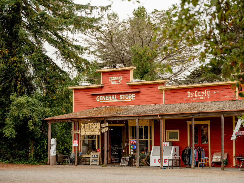Duncans Mills General Store is a red clapboard building with hand-written signs and an ice machine in front. 