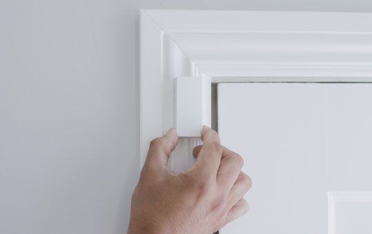 A hand placing the contact on the door frame