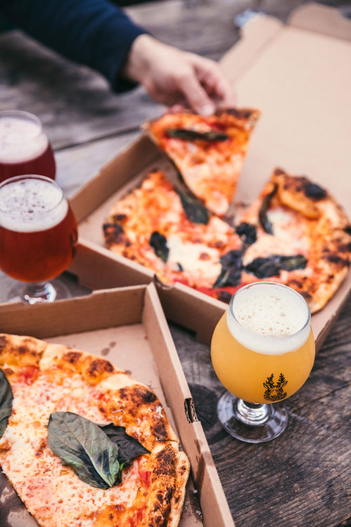 Wood-fired pizzas in boxes topped with basil. 