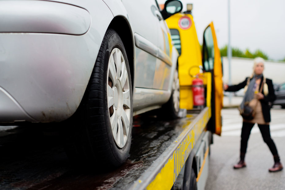 A woman gets in a tow truck after her car was loaded onto the bed.