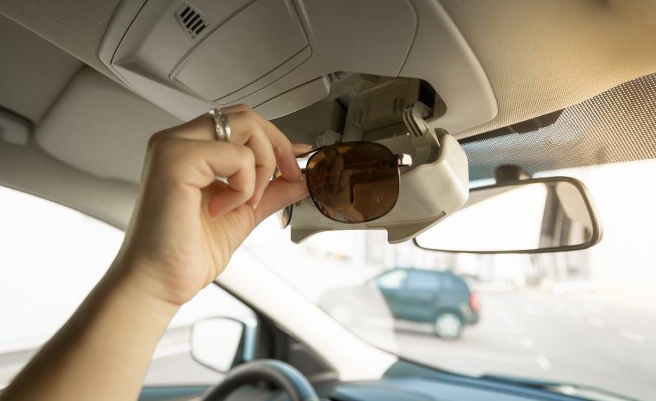 A woman removes her sunglasses from the holder in the roof of the car.
