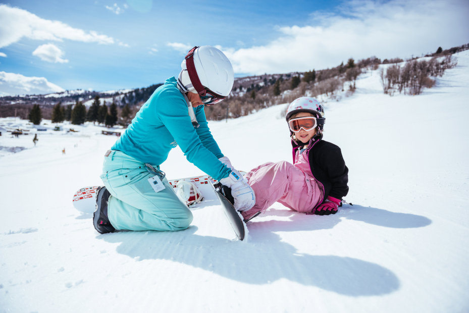 A woman helps a little girl put her boot back into her snowboard on the slope at Nordic Valley Ski Resort in Ogden, Utah.