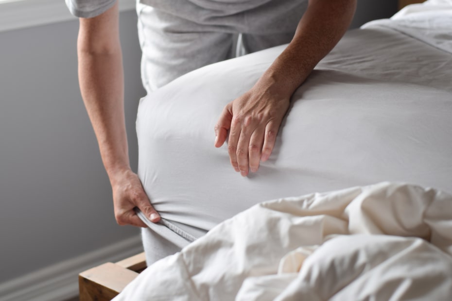 A traveler removes bedding from a mattress to check for bed bugs.