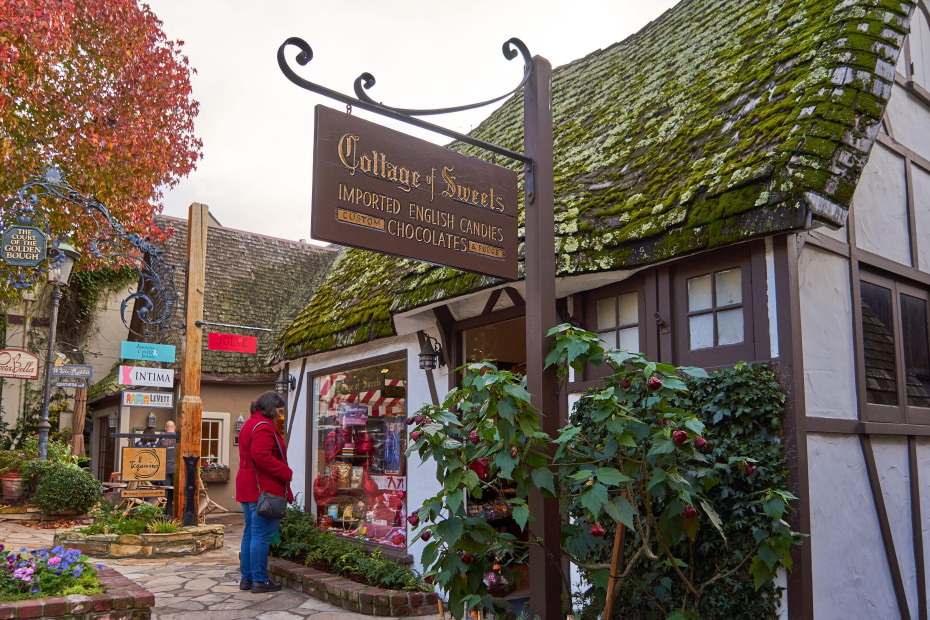 A woman in red coat looks at the window display of candy and sweets of the Cottage of Sweets shop in Carmel-by-the-Sea in California.