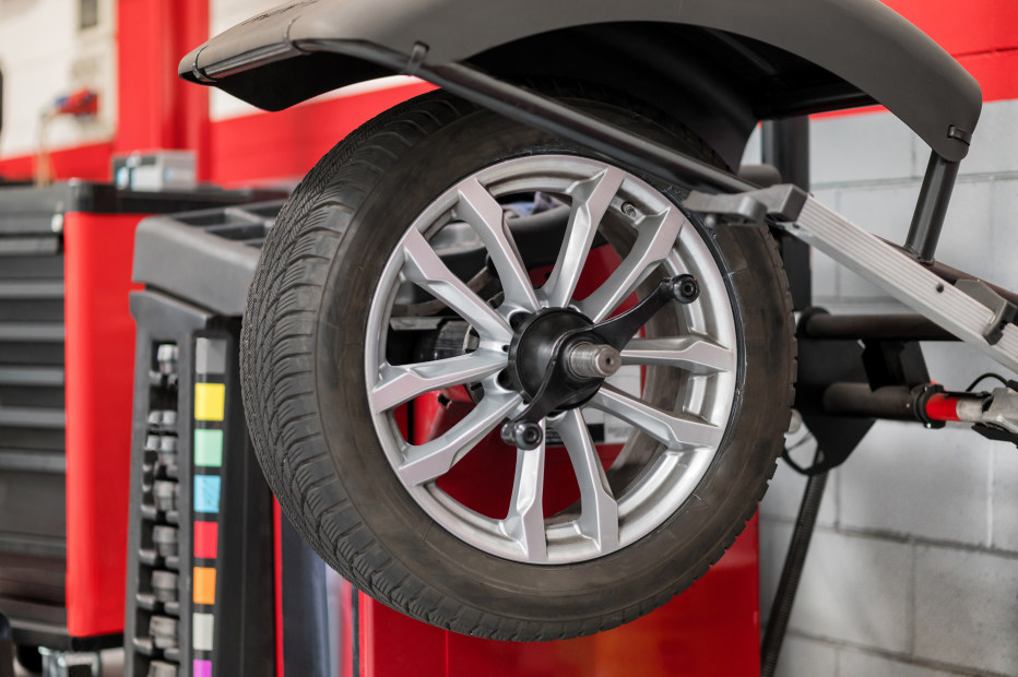 Wheel hanging on wheel balancer inside a car repair shop.