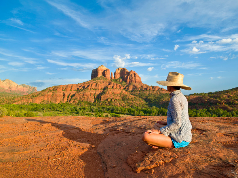 A woman sits on a red rock on a hike in Sedona, Arizona.