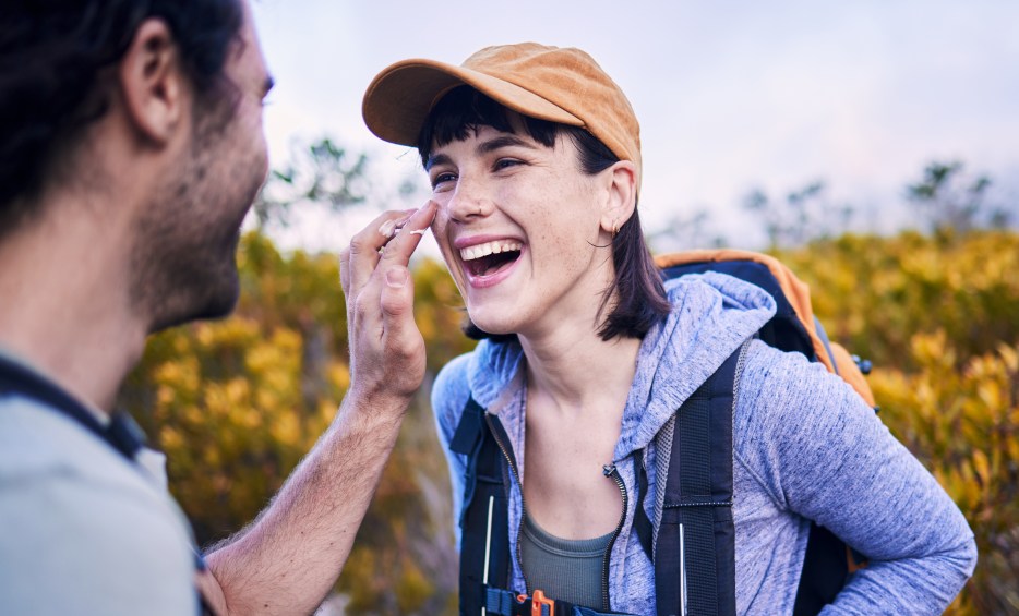 A man applies sunscreen to his partner's face out on a trail.