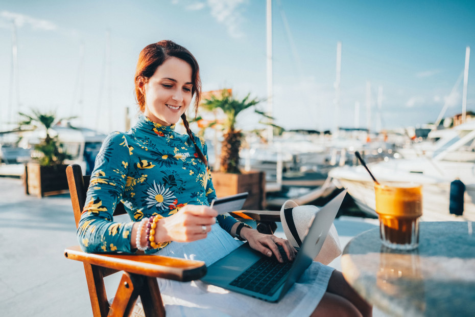 A woman pays with her credit card while sitting on a dock with her computer.