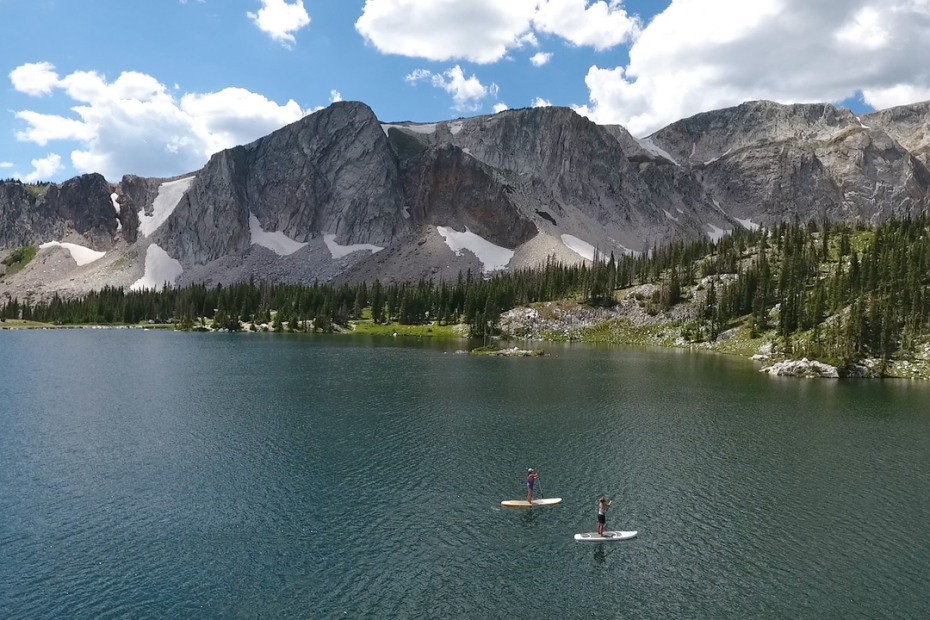Two people stand-up paddle board on Mirror Lake near the base of Medicine Bow Peak.